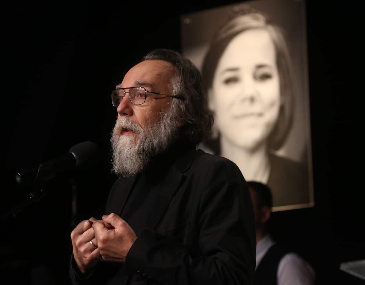 Alexander Dugin speaking at his daughter Daria's funeral. There is a picture of a daughter behind him.