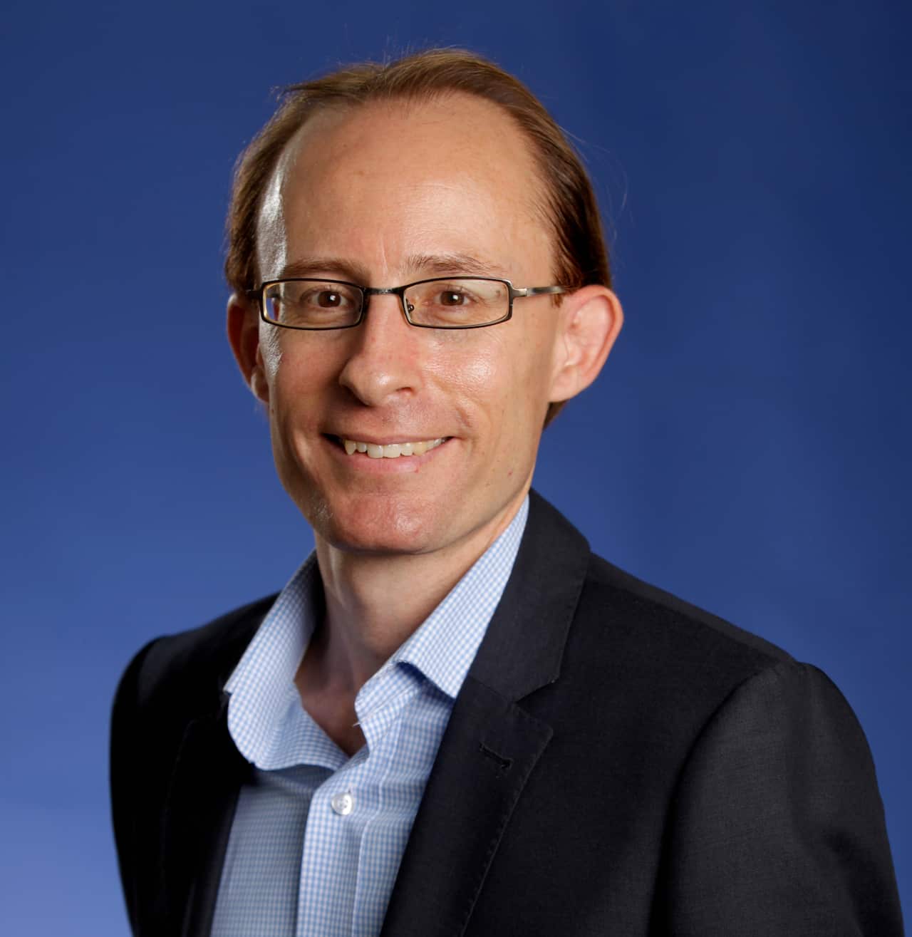 A man in a black blazer and collared shirt is smiling 