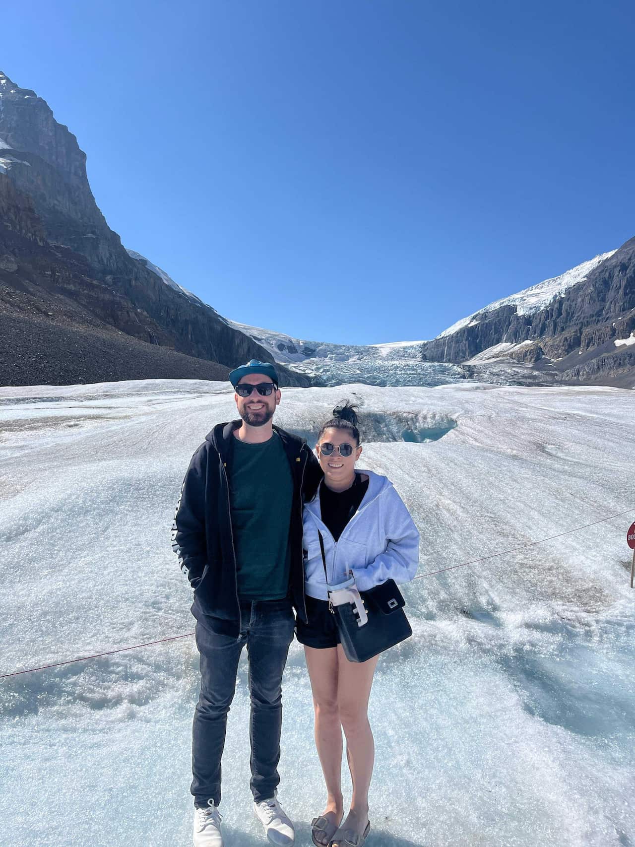 A male and female couple stand in front of a glacier in Canada.