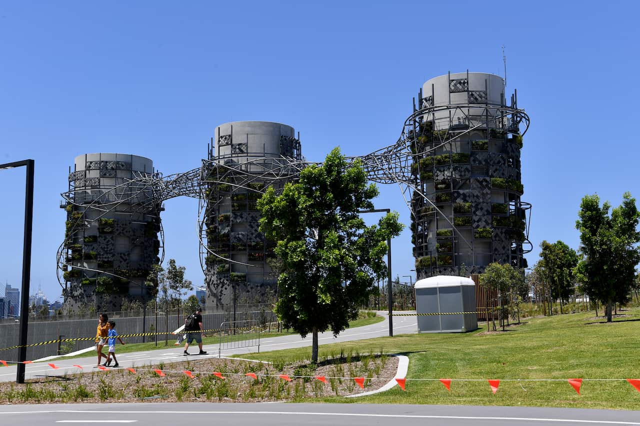 Fenced-off parklands, with people walking down pavement.