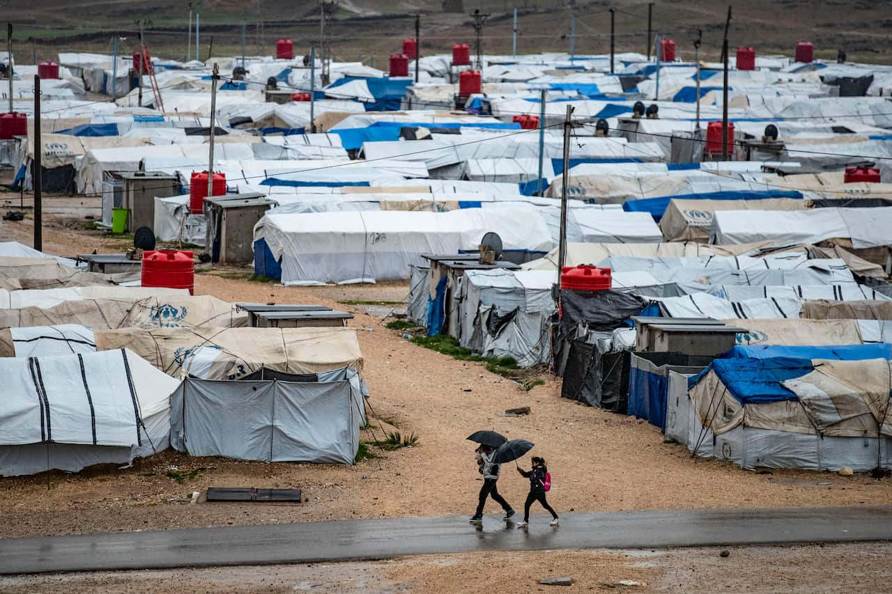 People using umbrellas as they walk outside at a detention camp.