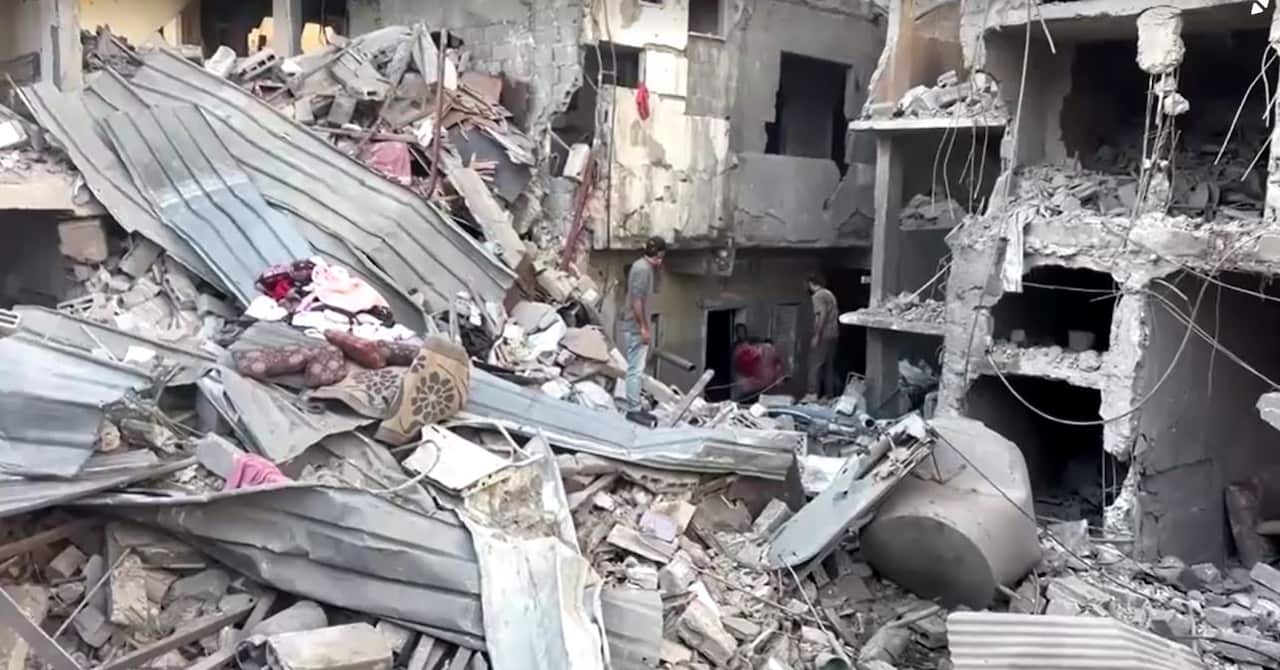 Three people surrounded by piles of rubble and damaged buildings