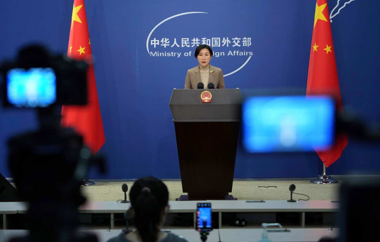 Woman stands at a lectern in front of Chinese flags.