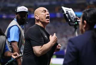 Egypt's coach in a black t-shirt yelling and holding his shirt on the side of a football pitch
