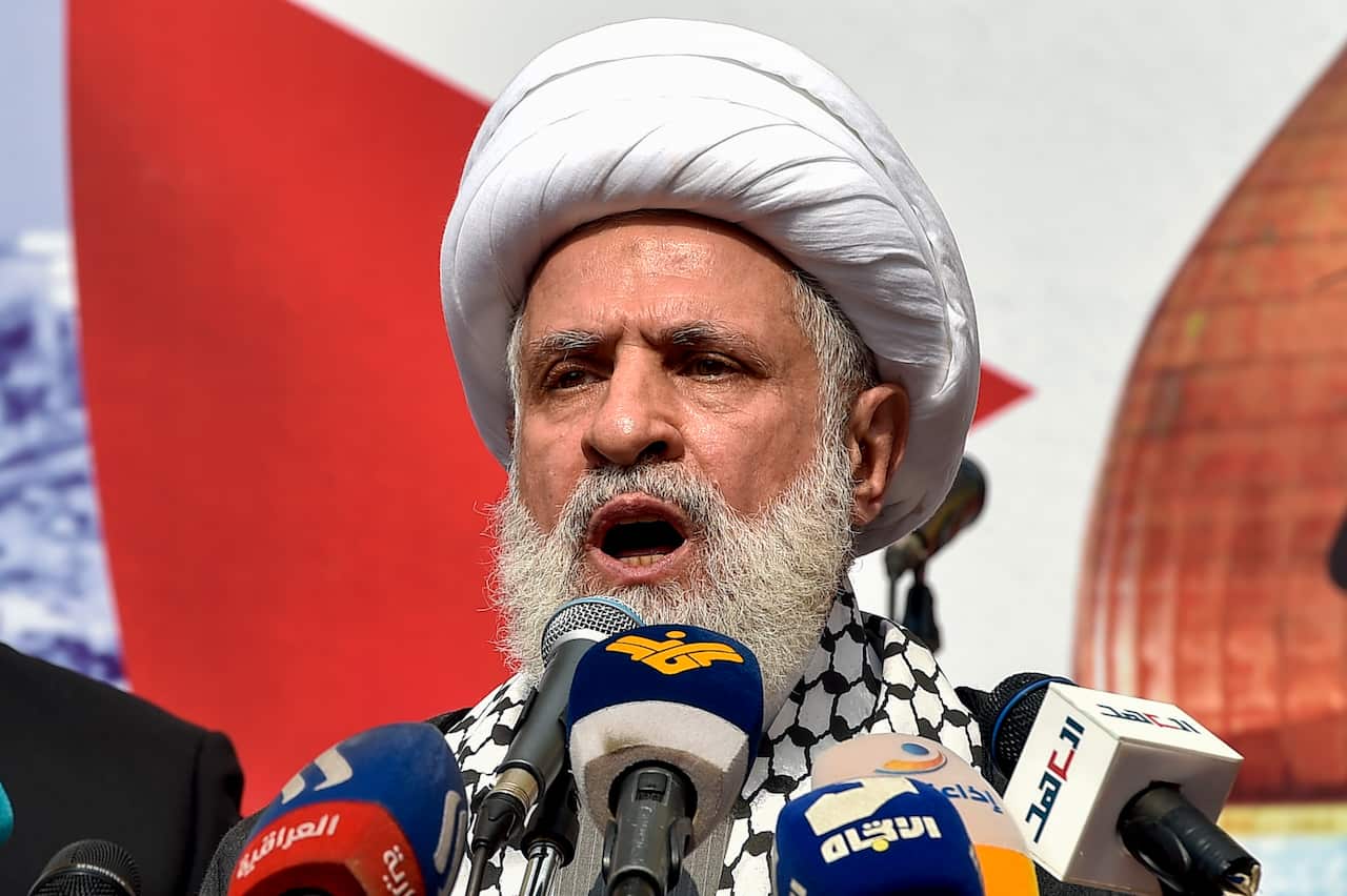 A man in a white turban is speaking into microphones.