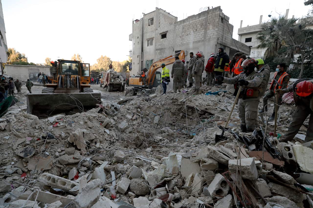 People standing on rubble. A bulldozer pushes some of the debris