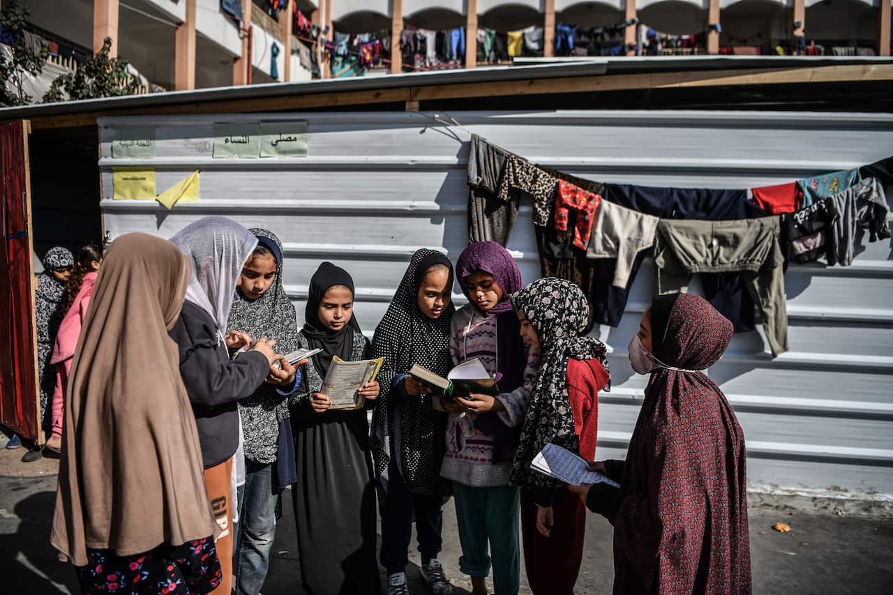 A group of Palestinian girls stand in a semicircle reading the Quran