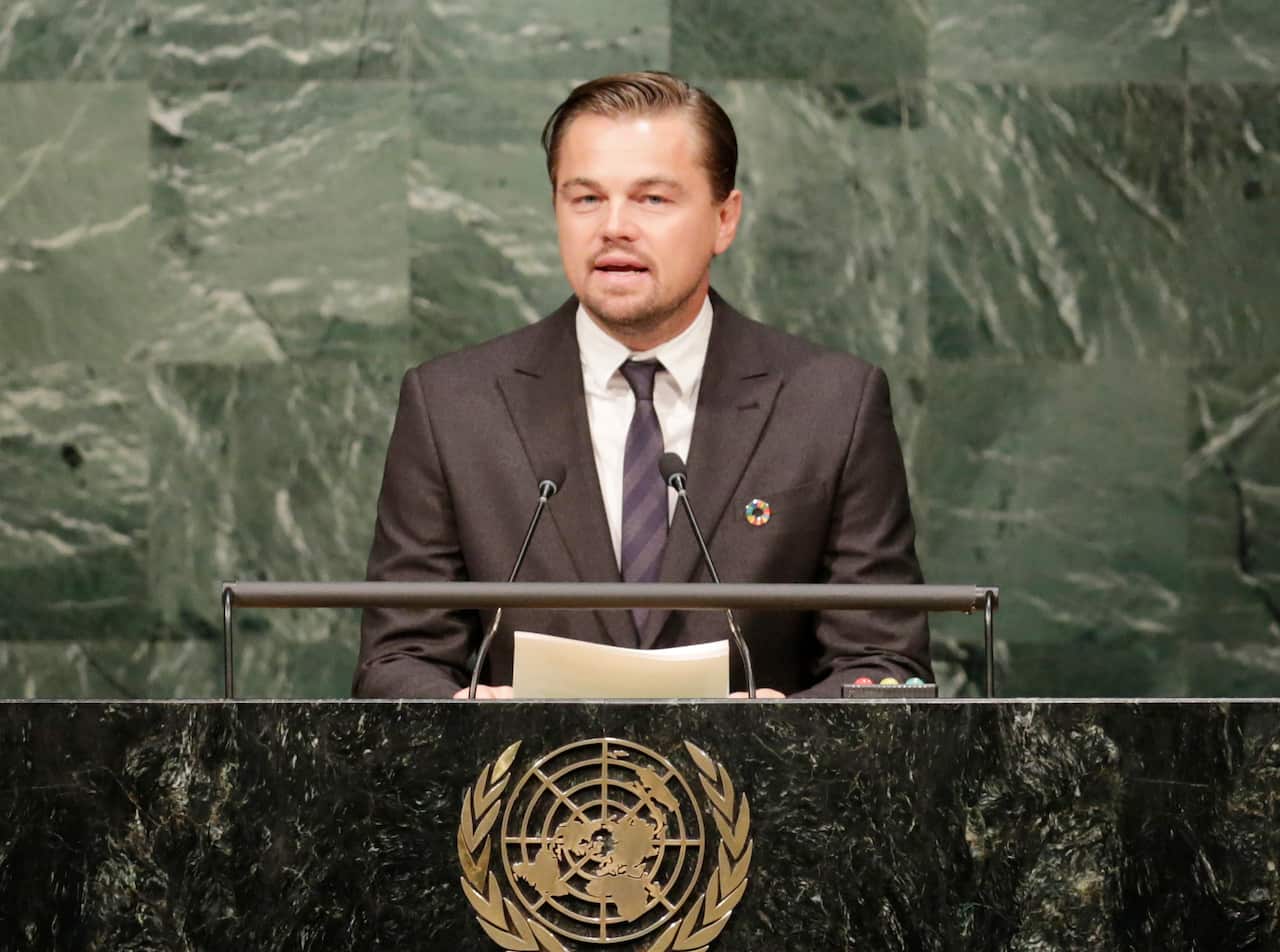Leonardo Di Caprio speaking at a podium with a United Nations emblem.