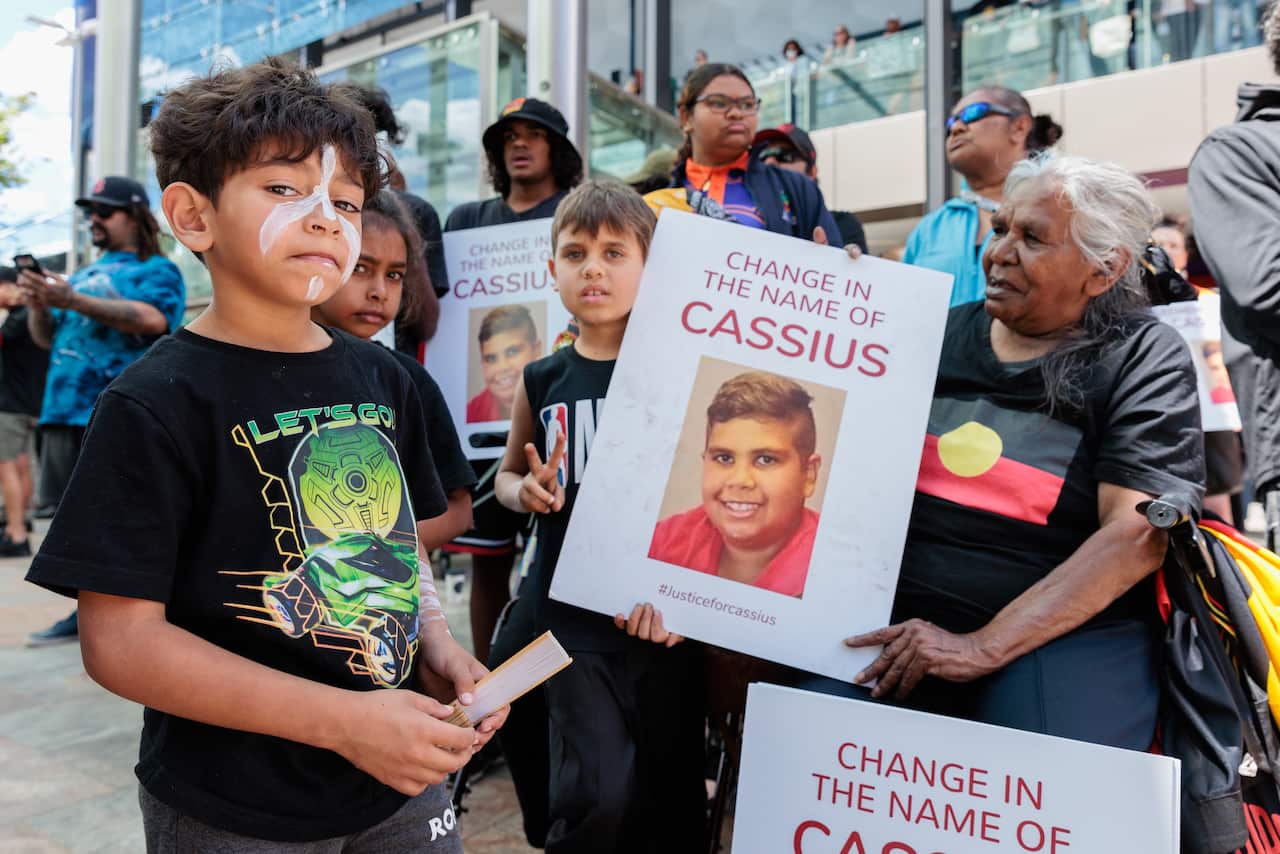 A group of young children and an older women hold up signs during a vigil for Cassius Turvey