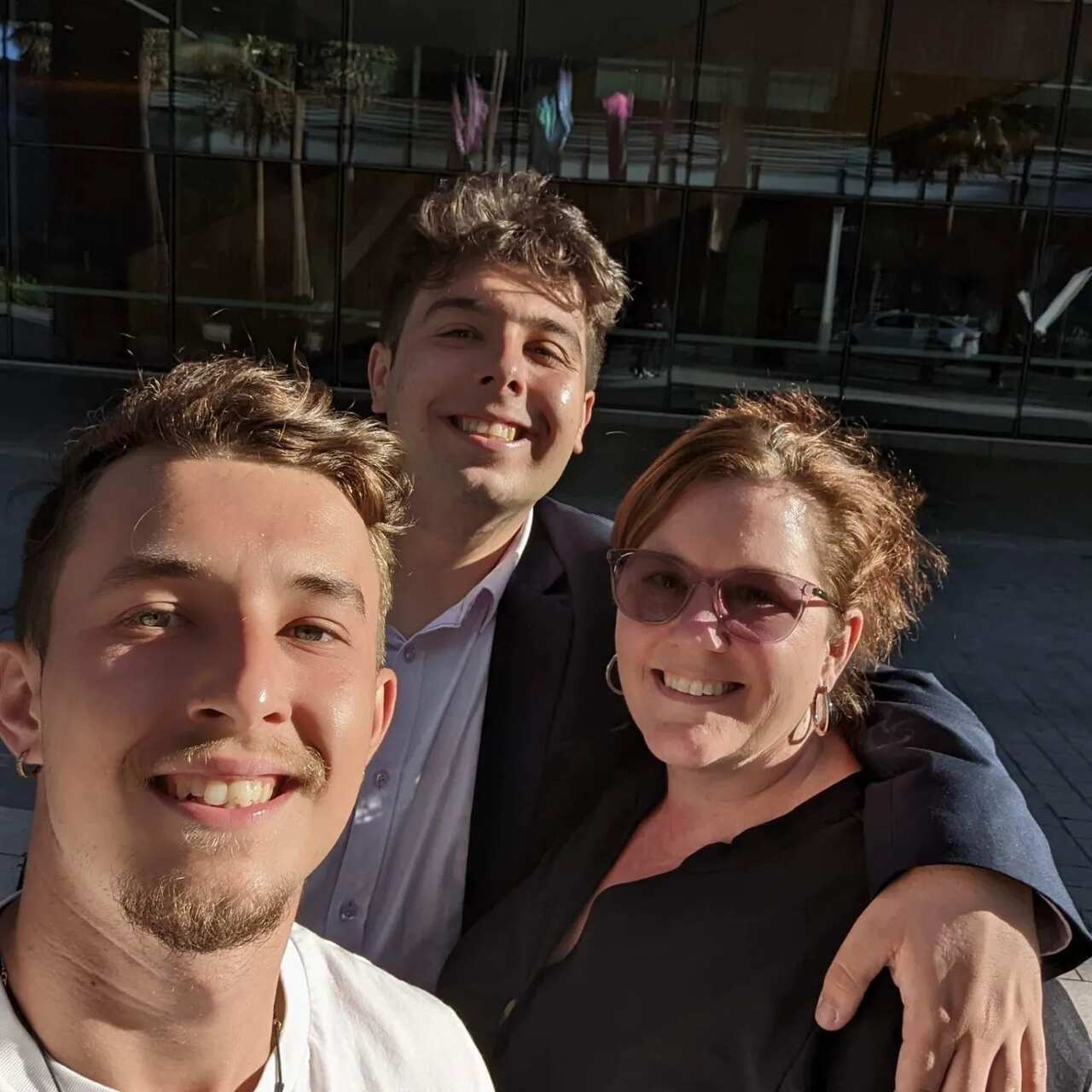 A woman with two teenage boys. One has his arm around her shoulder. All are smiling. 