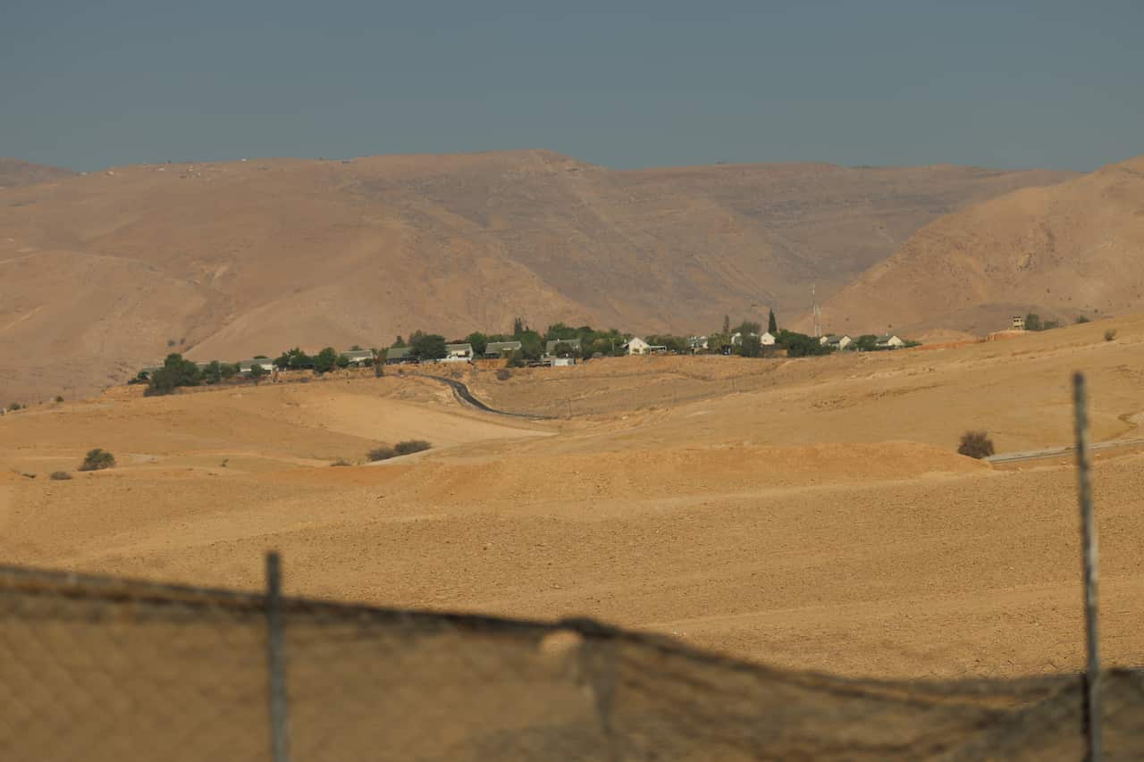 A small settlement with green trees, photographed from the distance. It is set against desert and rocky mountains. 