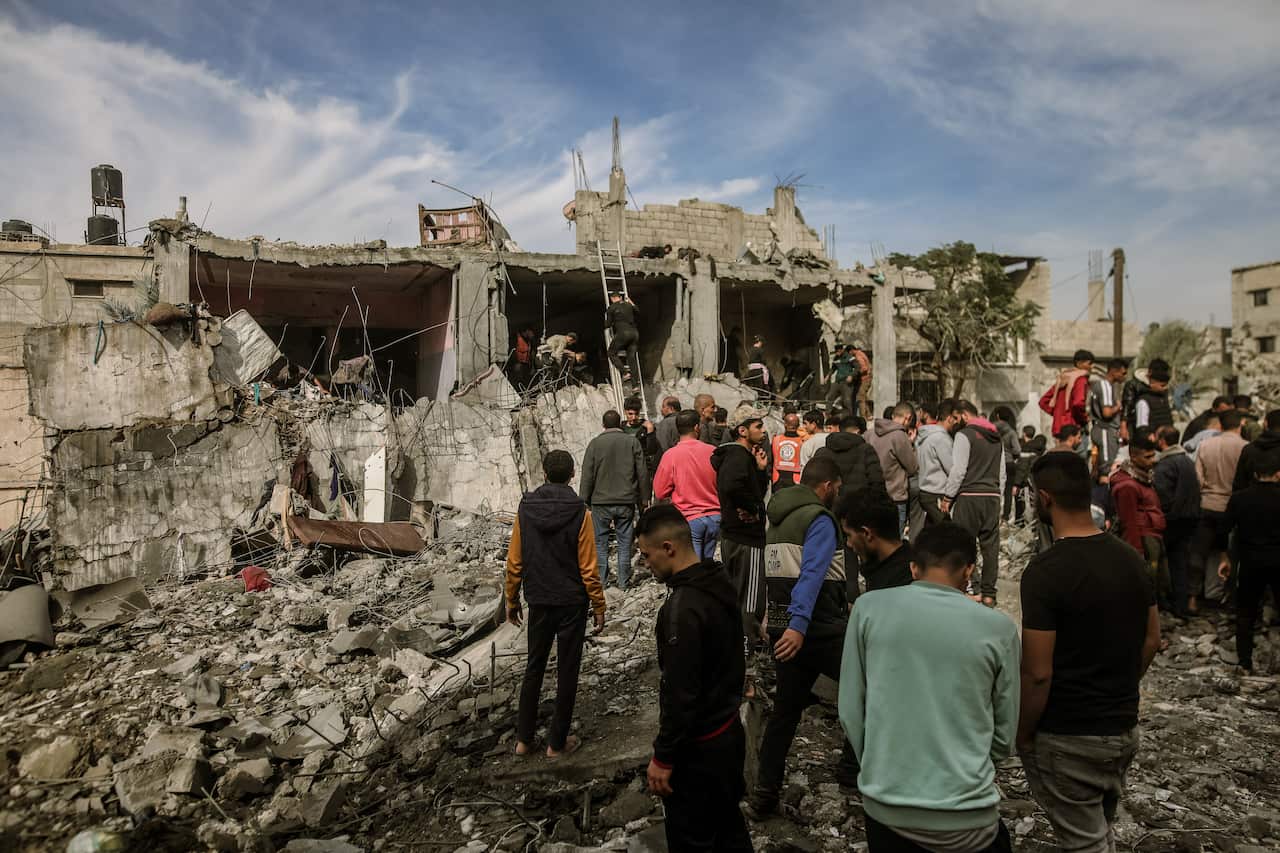 People gather in front of a destroyed building. 