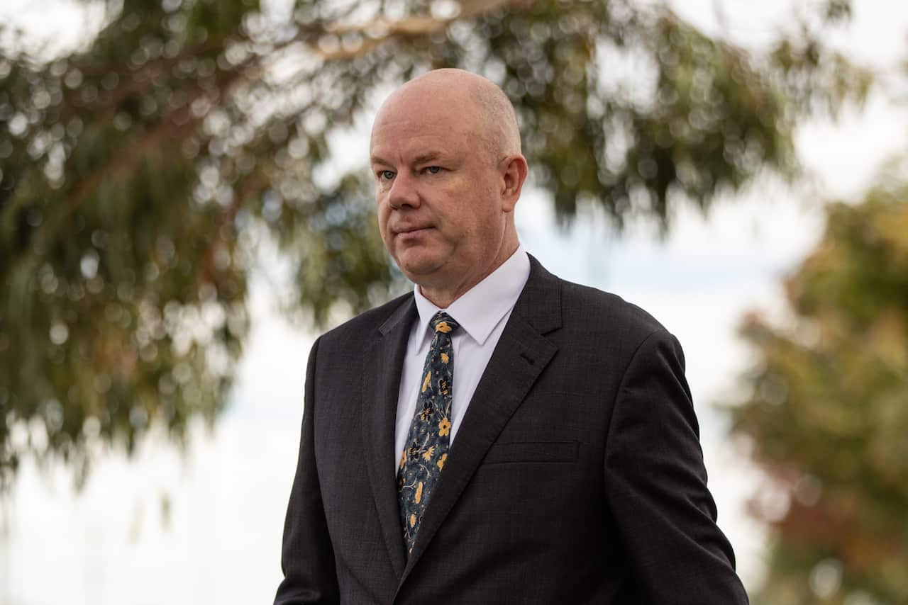A man in a black suit and a tie is walking outside.