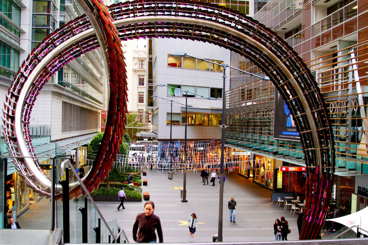 An open space in between shops with public art in the shape of a swirl.