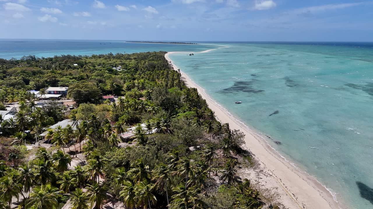 A drone shot of Masig Island, covered in trees and surrounded by aqua blue ocean.
