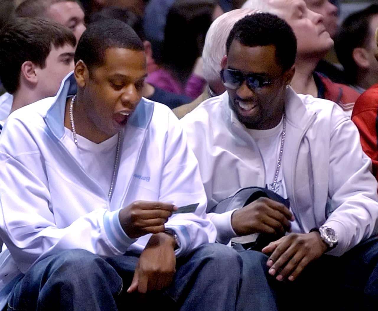 Jay-Z (left) and Sean Combs sitting next to each other. Both are wearing white jackets