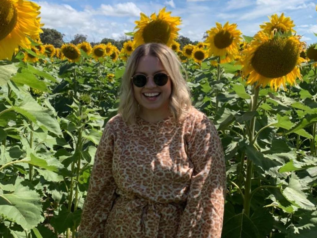 Woman standing in a field of sunflowers smiling.