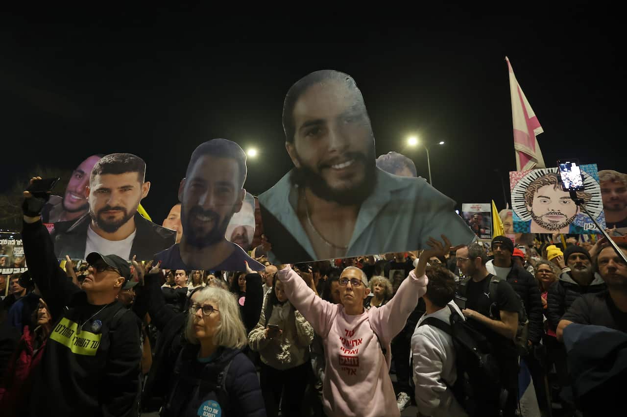 A crowd of people, some holding up large cutouts of men's faces and others holding flags.