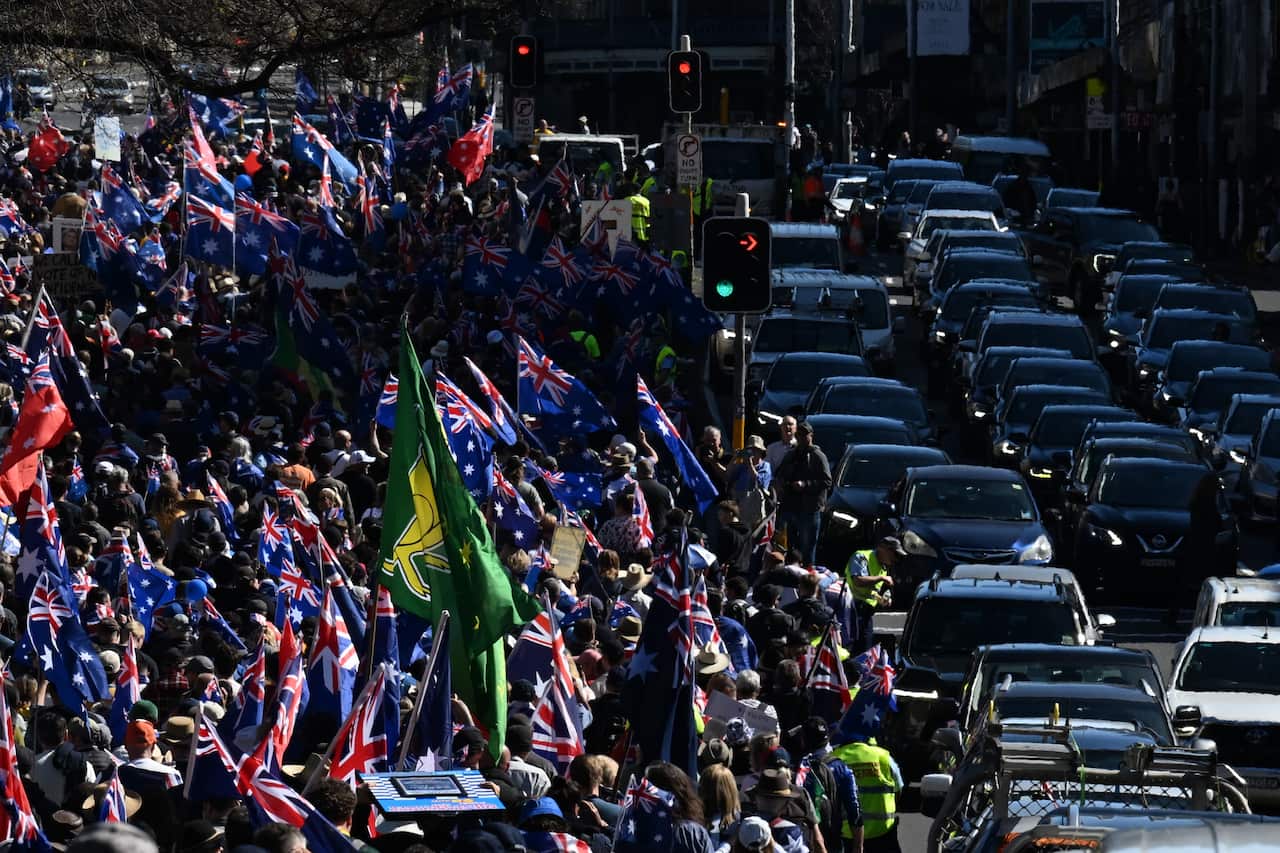 A large group of people walking down a street, many waving Australian flags.
