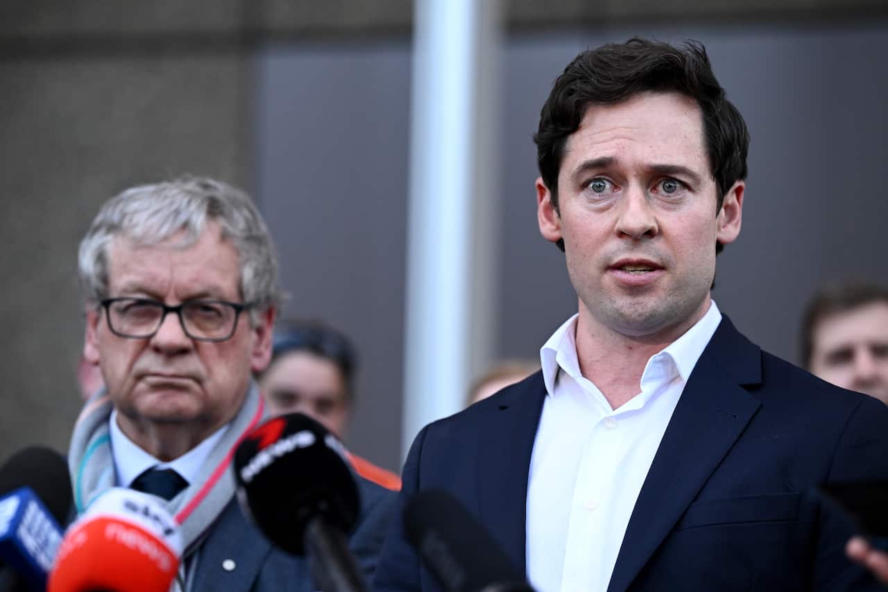 Two men stand in front of microphones.