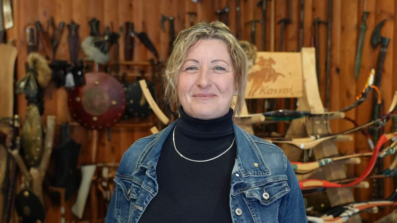 Una mujer blanca de mediana edad con cabello rubio. Ella está sonriendo y lleva una chaqueta vaquera y un top negro. 