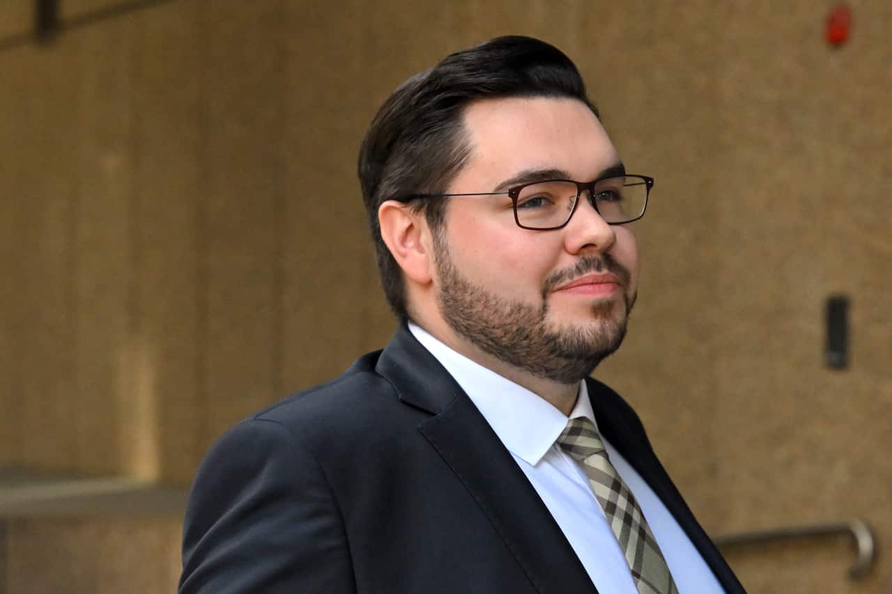 A man wearing a suit and tie smiling in front of a brown wall