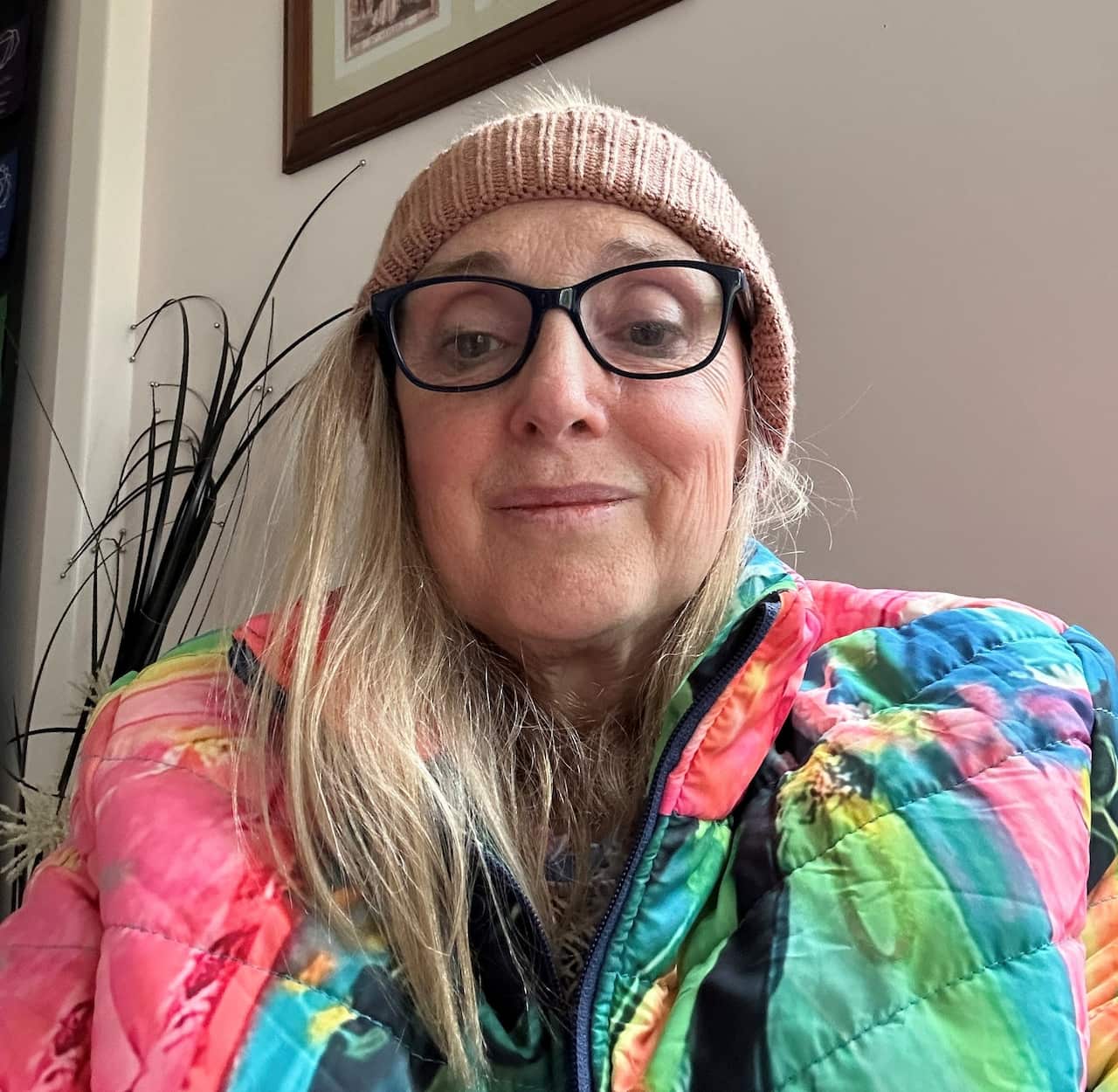 A selfie of a blonde woman wearing glasses and a colourful jacket.