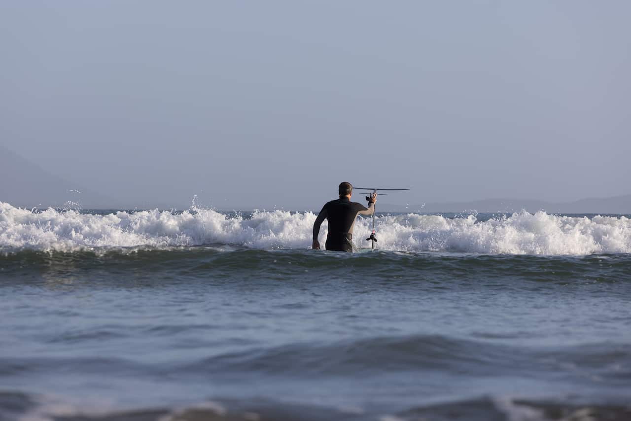 A man guides a surfboard with a hydrofoil attached into the waves.