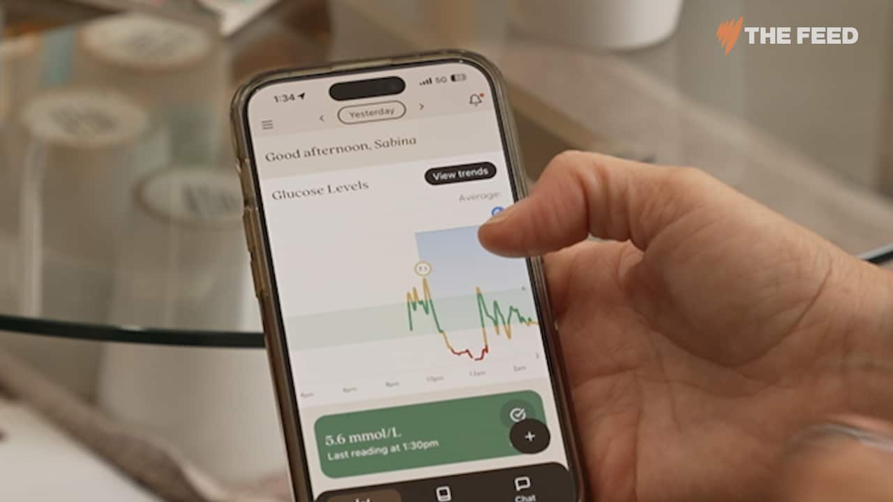 a woman is holding a phone that is showing a line chart with a line that is mostly green and a dip down into a red area in the middle