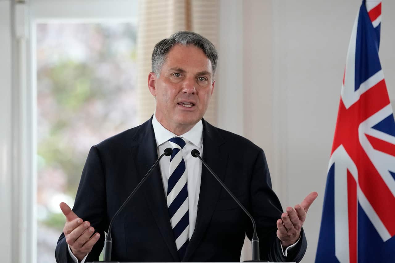Defence Minister Richard Marles is pictured speaking in front of a flag. 