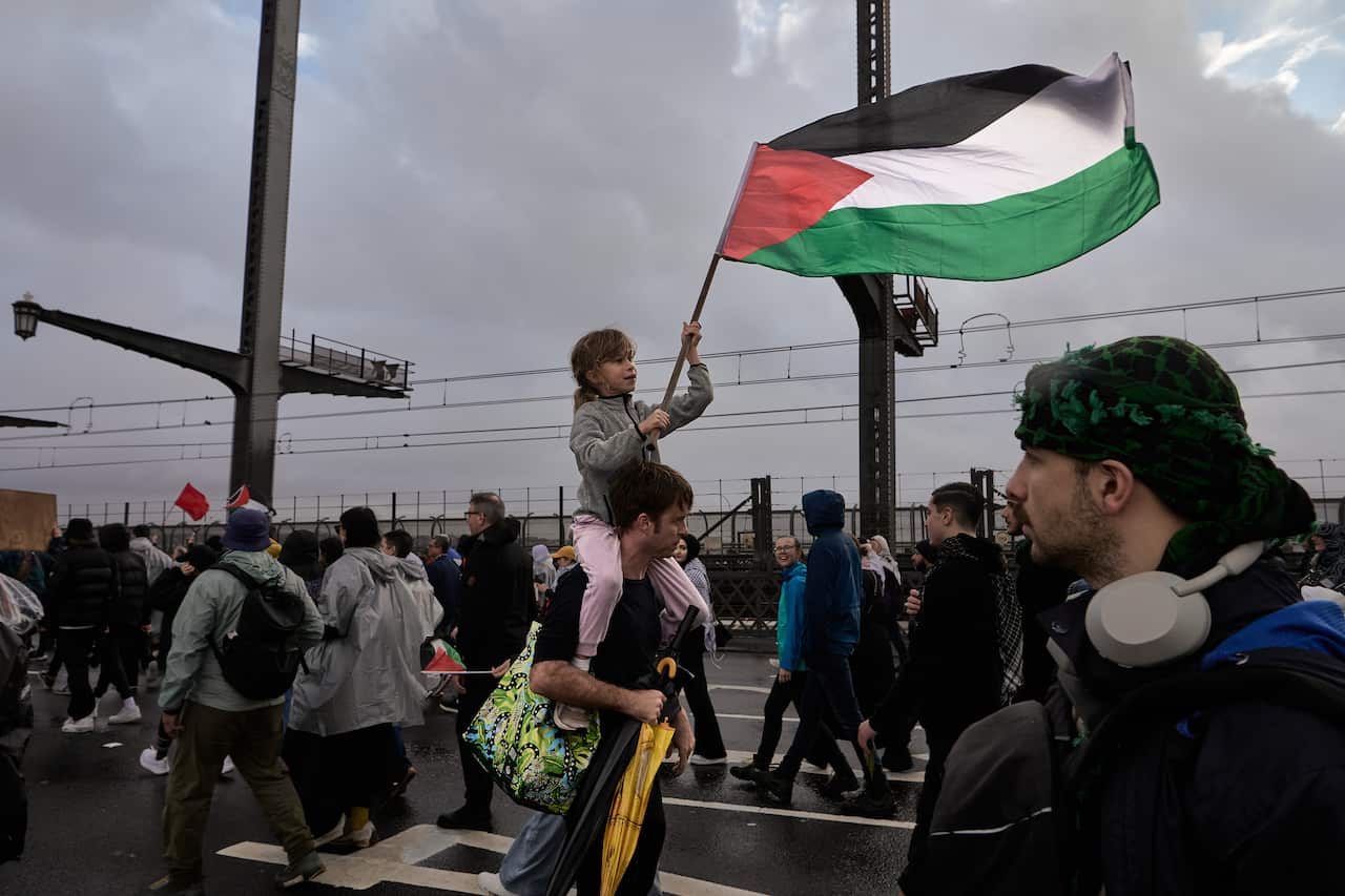 A young girl sits on a man's shoulders while waving the Palestinian flag.