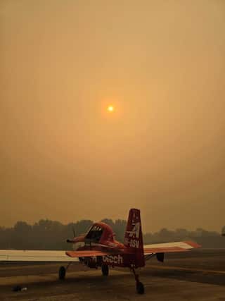 A red Fire Boss plane sits on the tarmac with the eerie orange haze of smoke covering the sky.