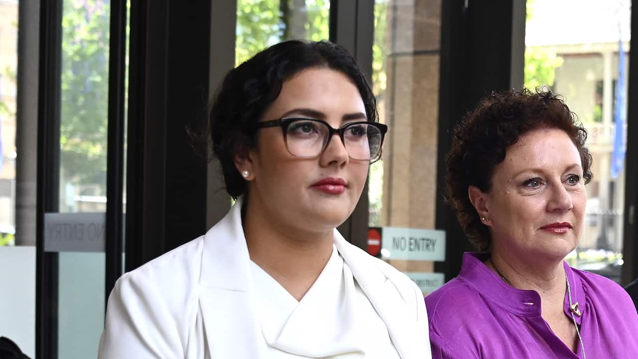 A woman wearing a white blazer next to a woman wearing a purple shirt.