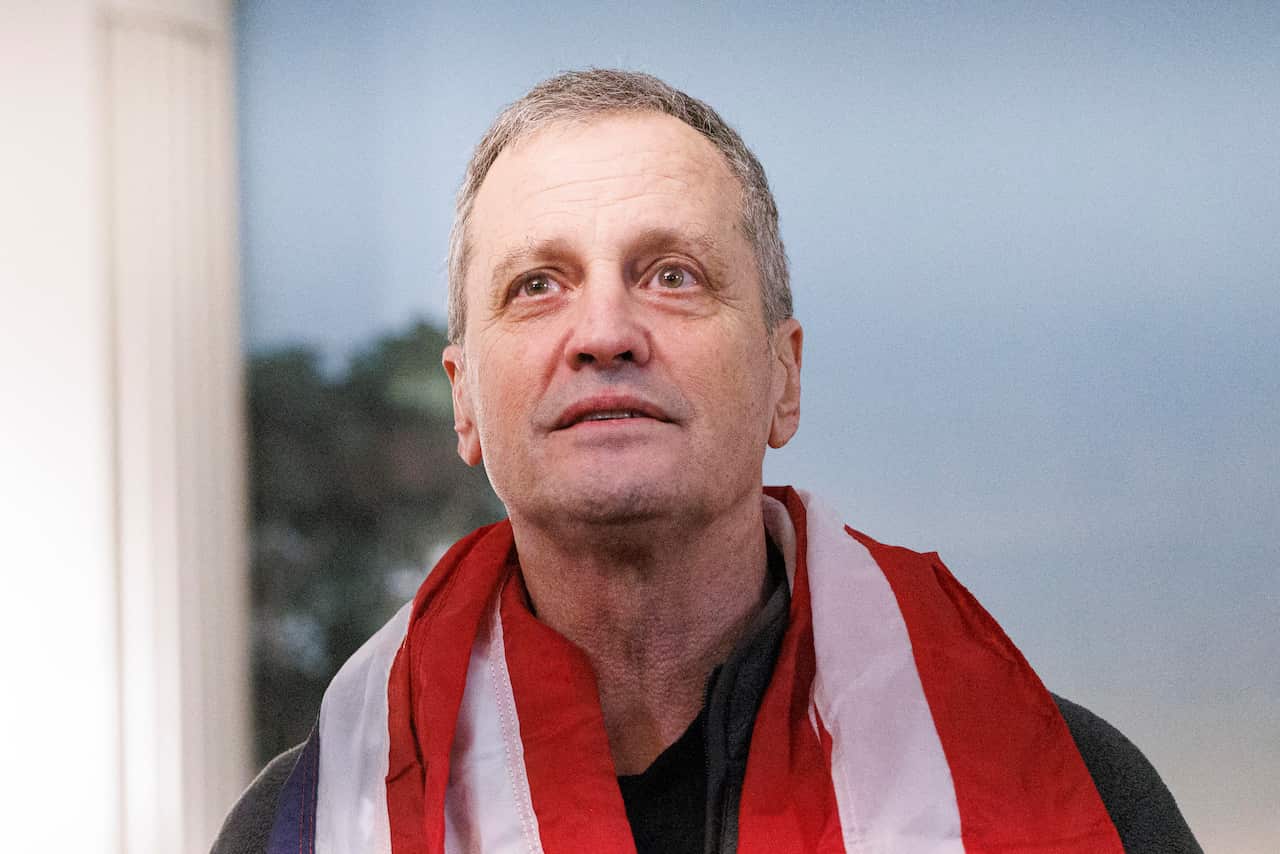 A man looks wistfully with an American flag draped around his shoulder.
