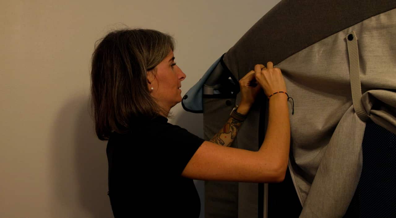 A woman is standing beside a large soft, grey structure, holding its zip. 