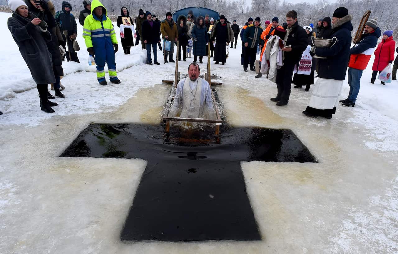 People are watching as a person dressed as a priest is dipping in the ice hole.