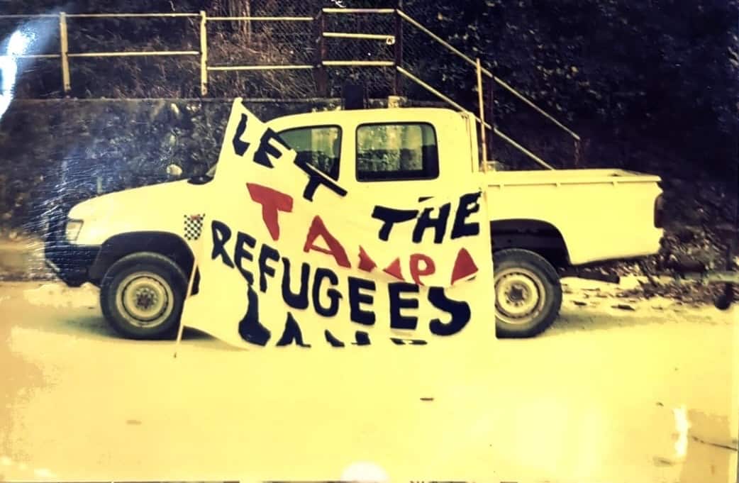 An old grayscale photo of a sign 'Let the Tampa refugees land' against a white ute marked in an open space at night.