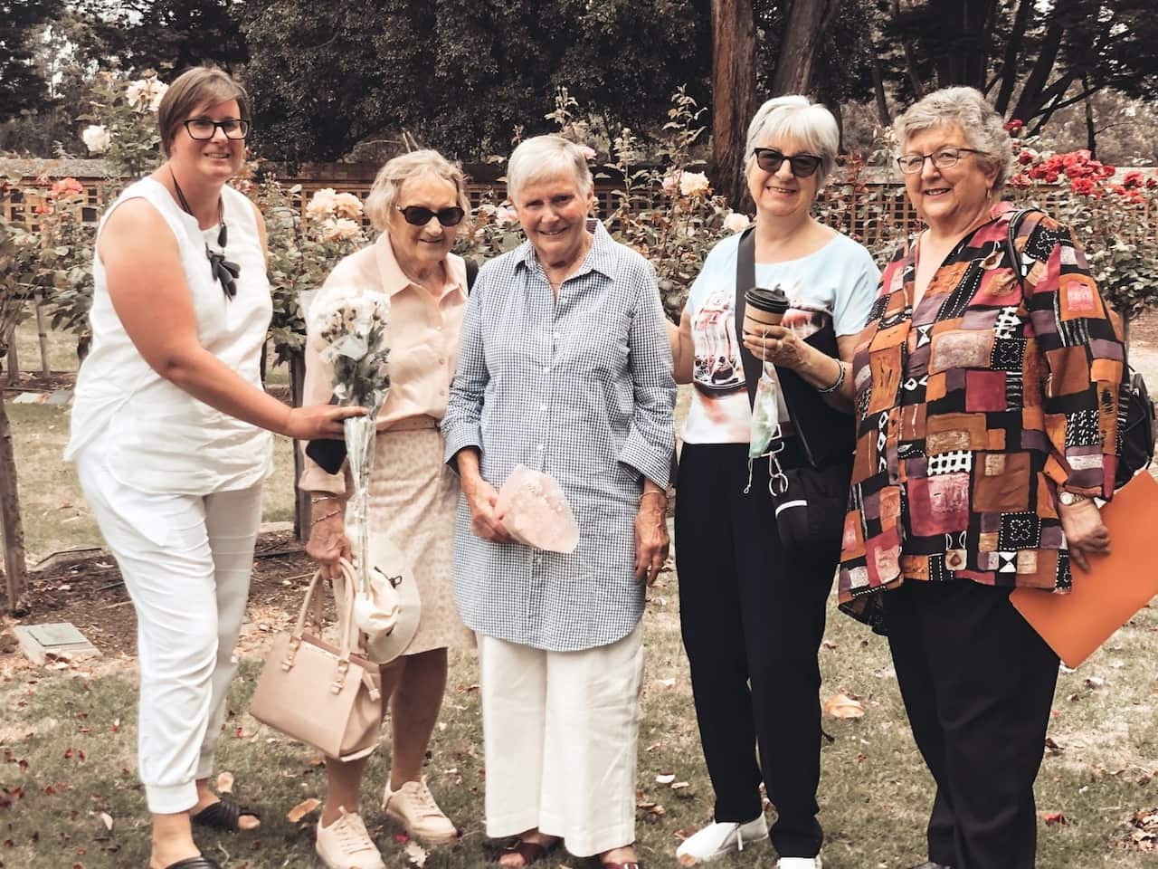 Fiver older women standing together, Joan Noonan on the right holds a document folder and another woman on the left holds flowers.