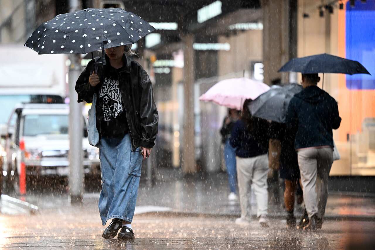 People holding umbrellas walk along a footpath as it rains.
