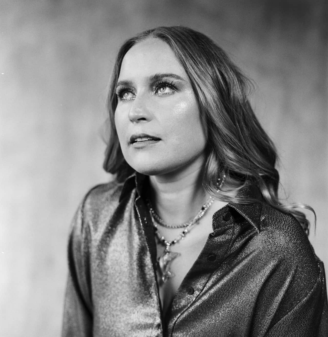 A grey-scale image of a woman wearing a sparkly button-up shirt and glittery makeup.