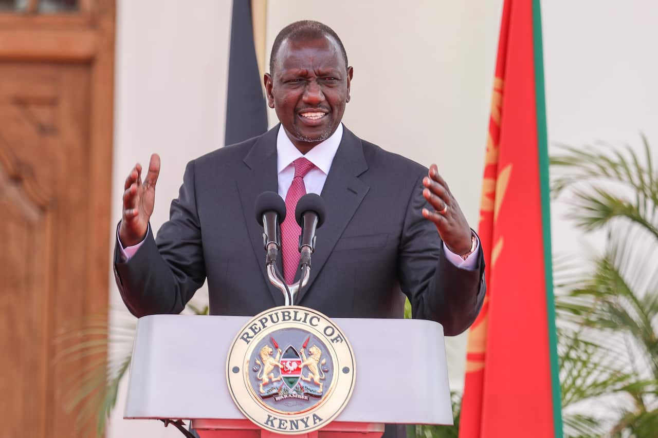 A man wearing a suit and tie standing at a lectern and speaking in front of microphones.