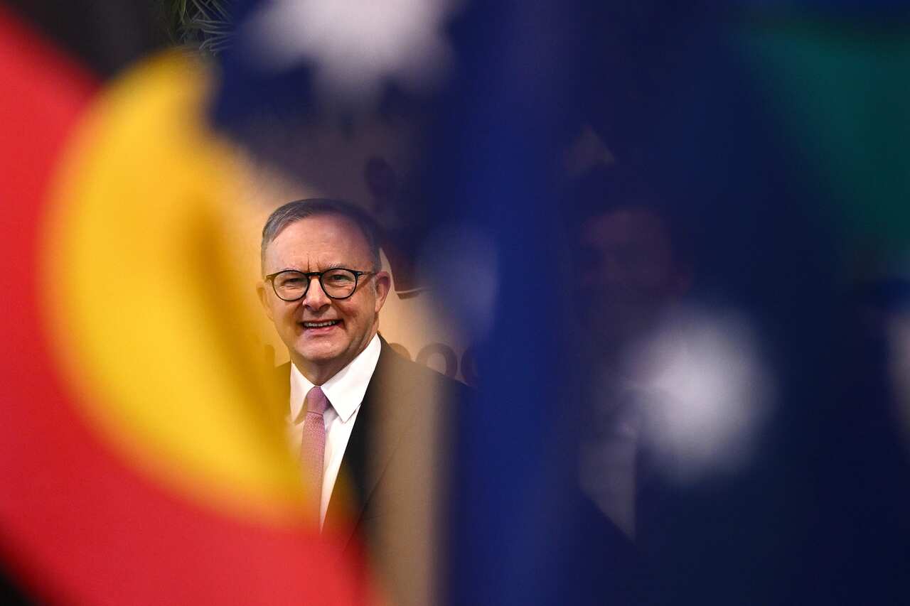 Anthony Albanese smiles, with Aboriginal and Torres Strait Islander flags in the foreground.