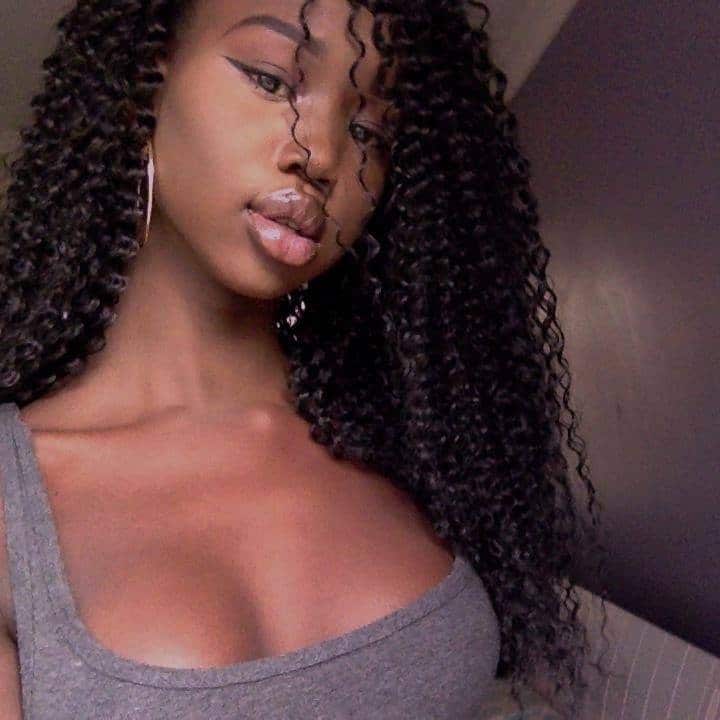 Woman with curly hair and grey singlet takes selfie. 