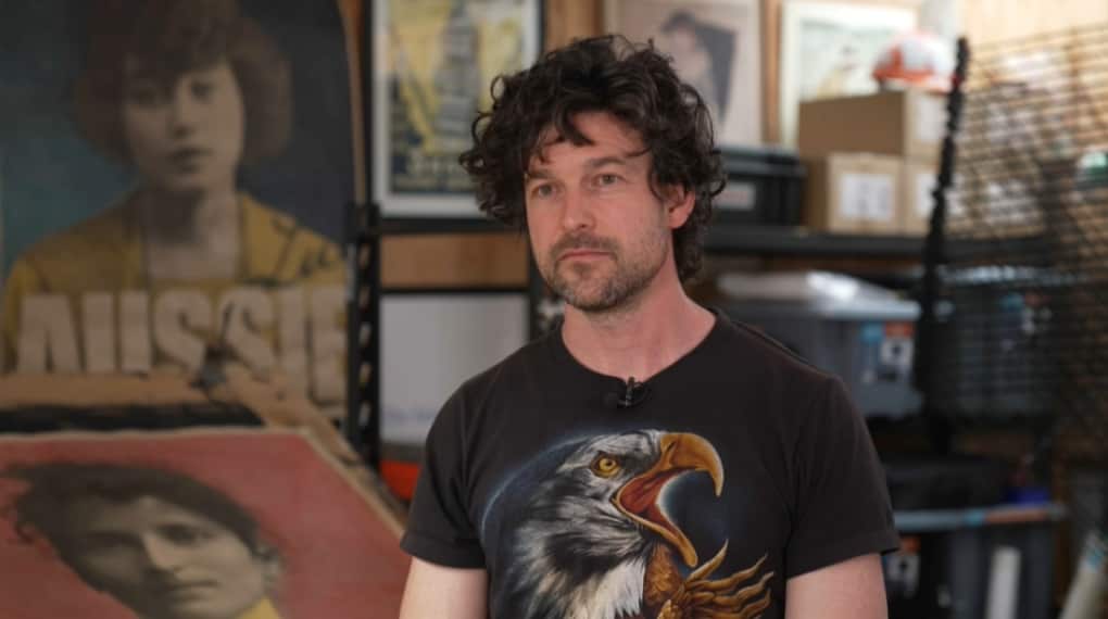 Peter Drew wearing a shirt with an eagle on it with what appears to be his art studio in the backdrop.