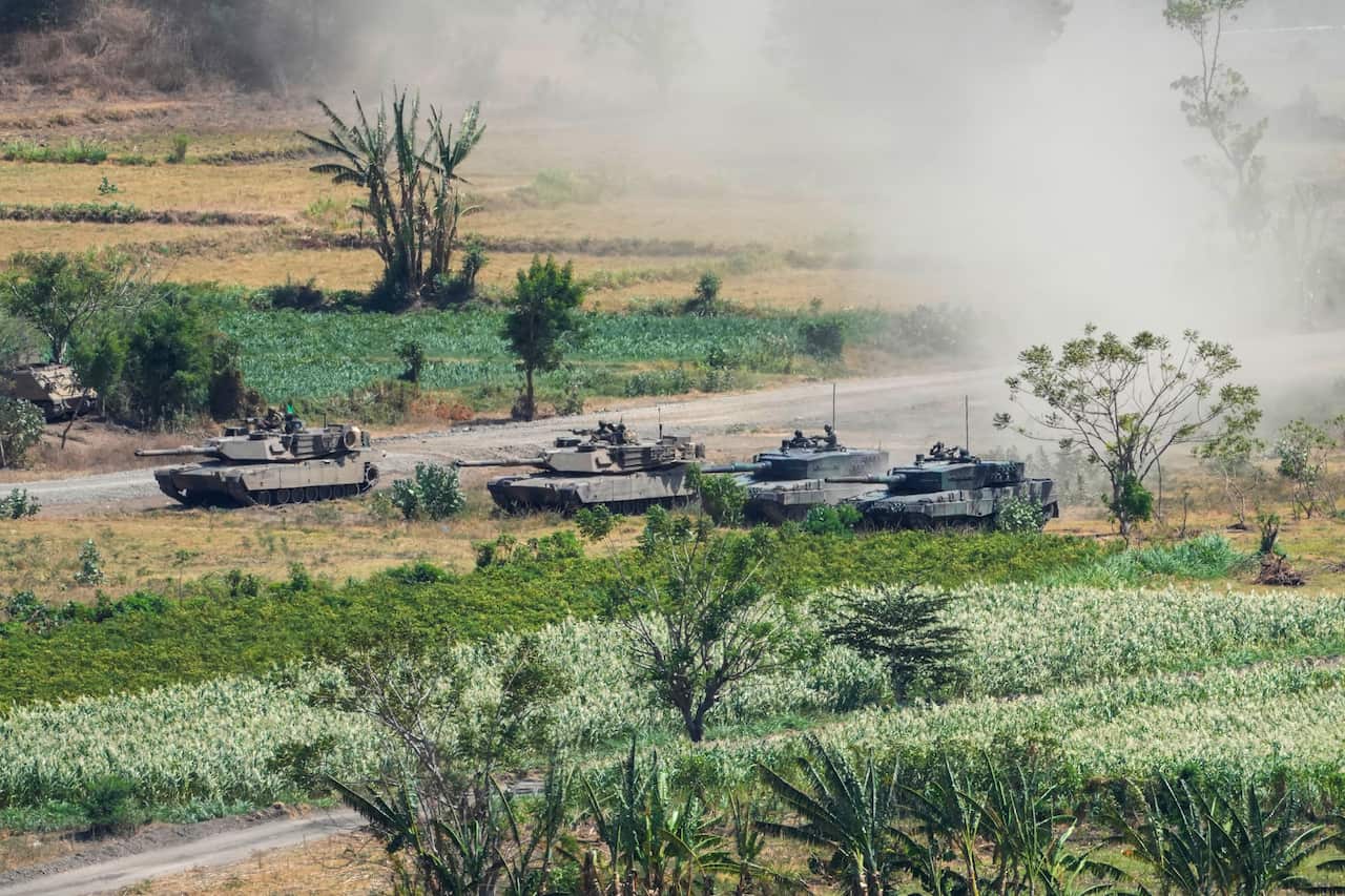 Four tanks drive side-by-side through a field.
