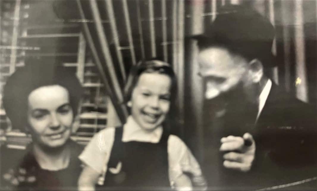 A child sits between a woman with black hair and a man with a black beard who is wearing a hat.