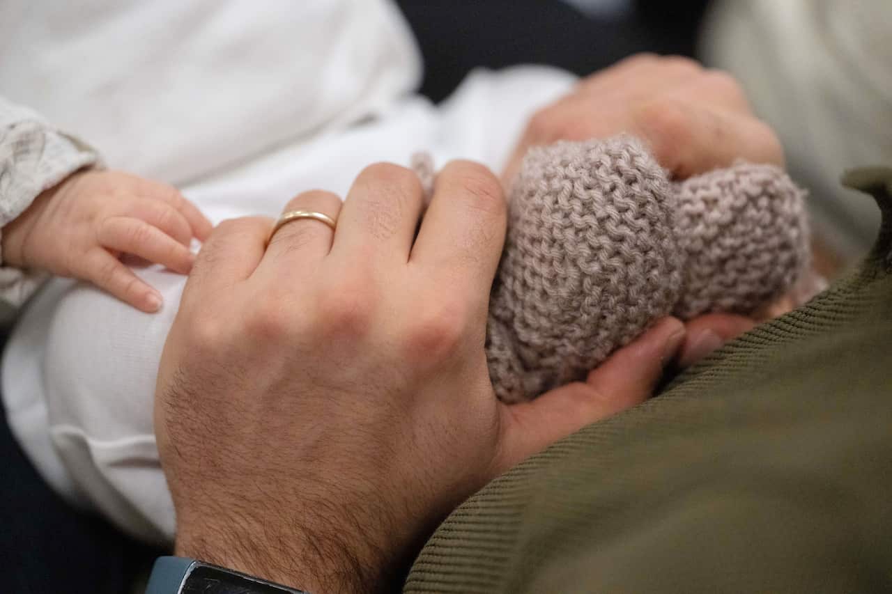 A man's hands are holding the little feet of a baby.