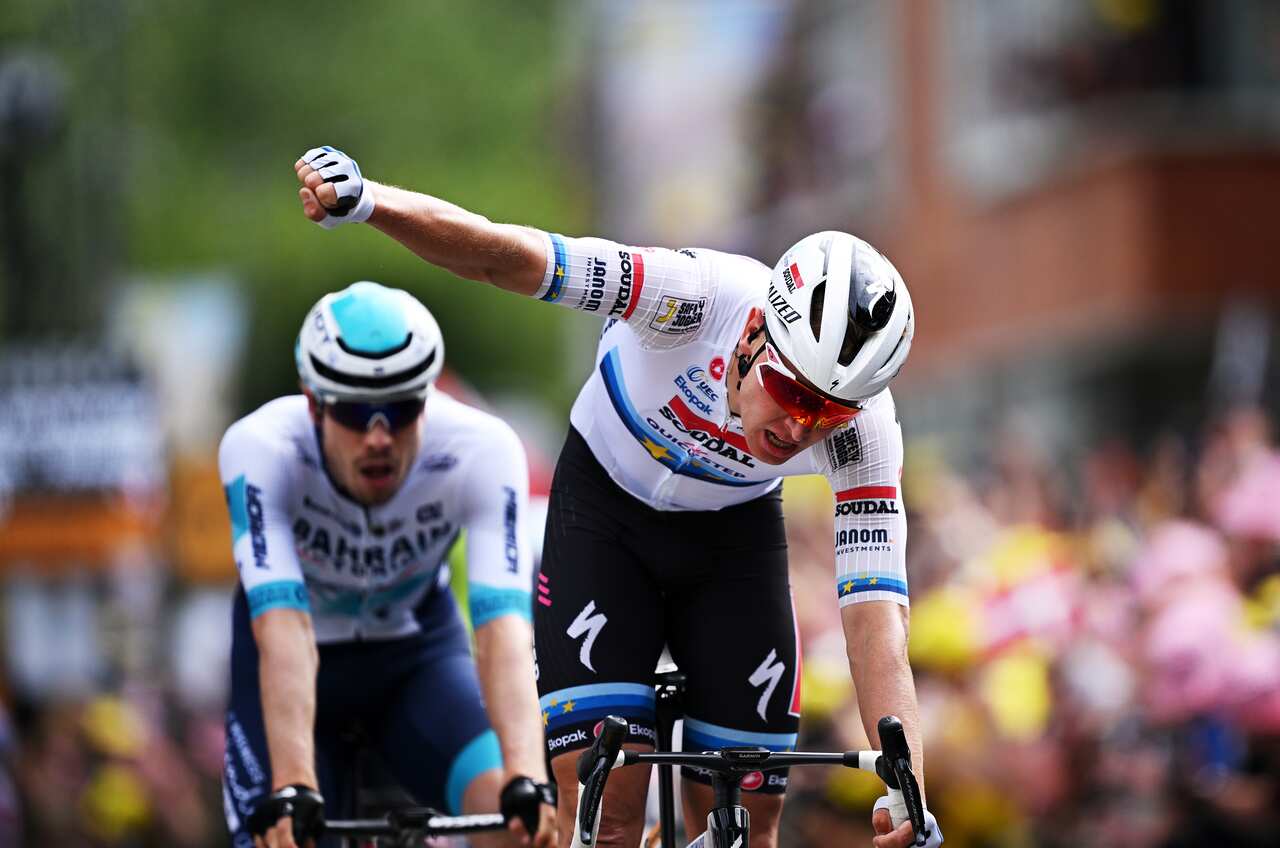 A cyclist raises his fist in celebration with another cyclist behind him.