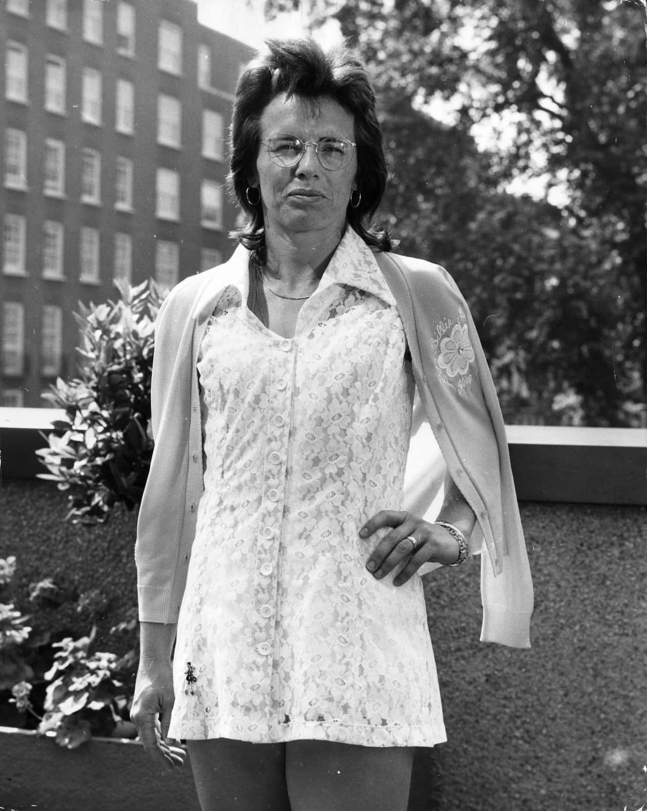 A black and white photo of a woman in white tennis clothes.