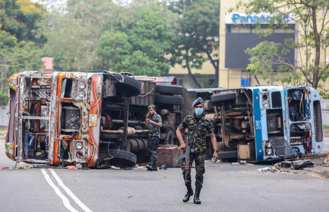 Armed Sri Lankan military personnel stand guard near burned vehicles 